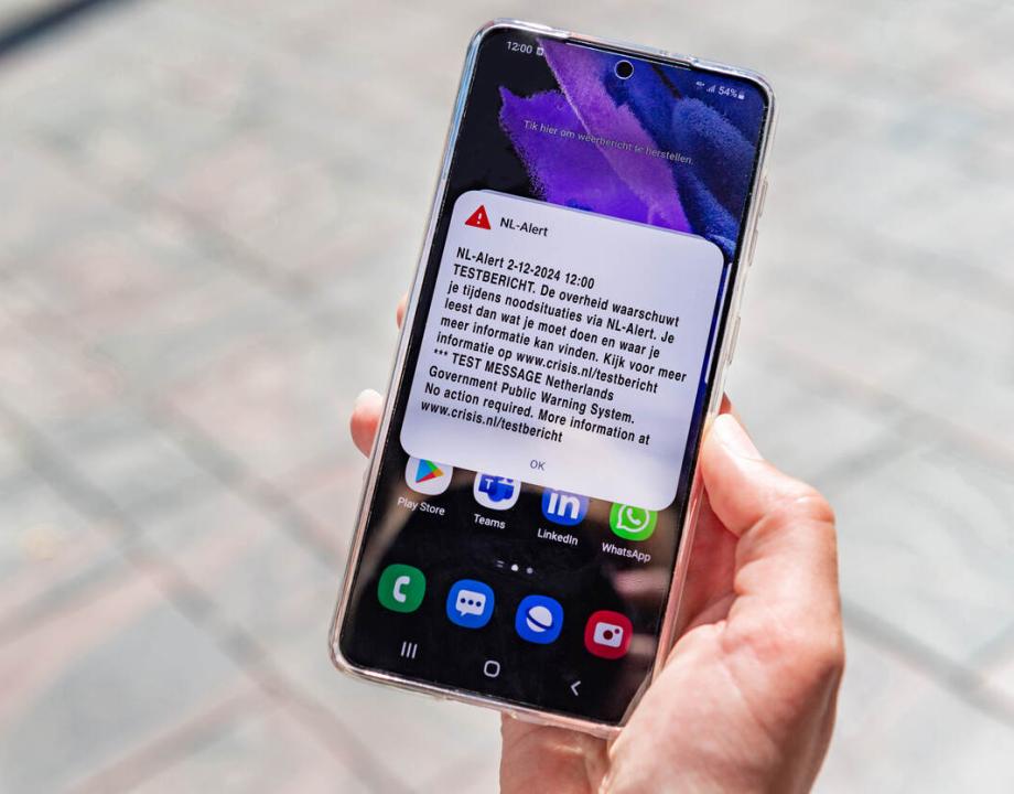 Mobiele telefoon in een hand met een test bericht van NL-Alert op het scherm