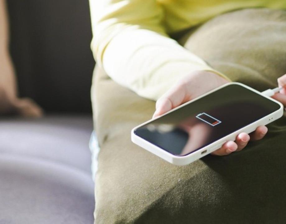 Vrouw zit op een bank die een oplaadkabel in een mobiele telefoon plaatst