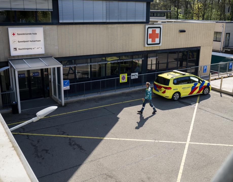 Ambulance staat voor een gebouw met een Rode kruis. Een GHOR medewerker loopt naar het gebouw .