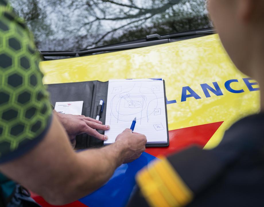 Een GHOR medewerker en een brandweerman staan voor een ambulance en overleggen wat te doen