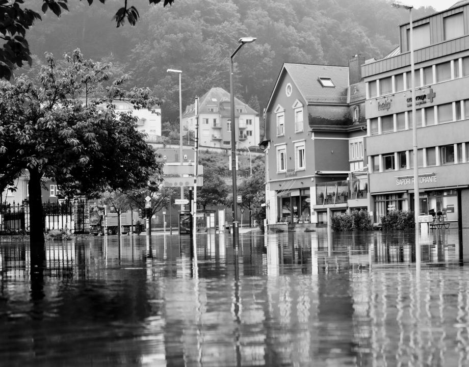 Foto in zwart-wit. Winkels en de straat staan onder water. Er is een overstroming